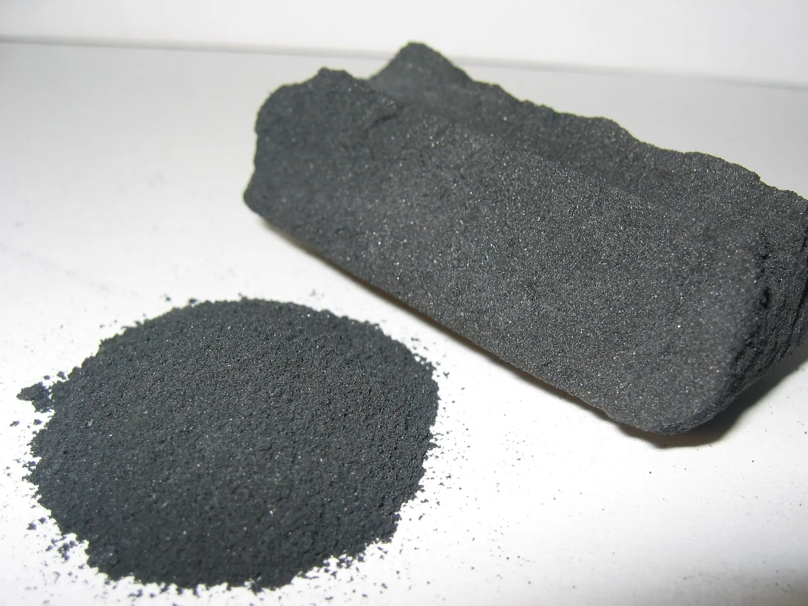 A block of activated carbon beside a small heap of the black powder.