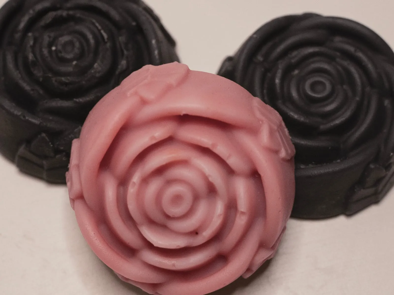 A pink rose-moulded soap in front of two black rose-moulded soaps.
