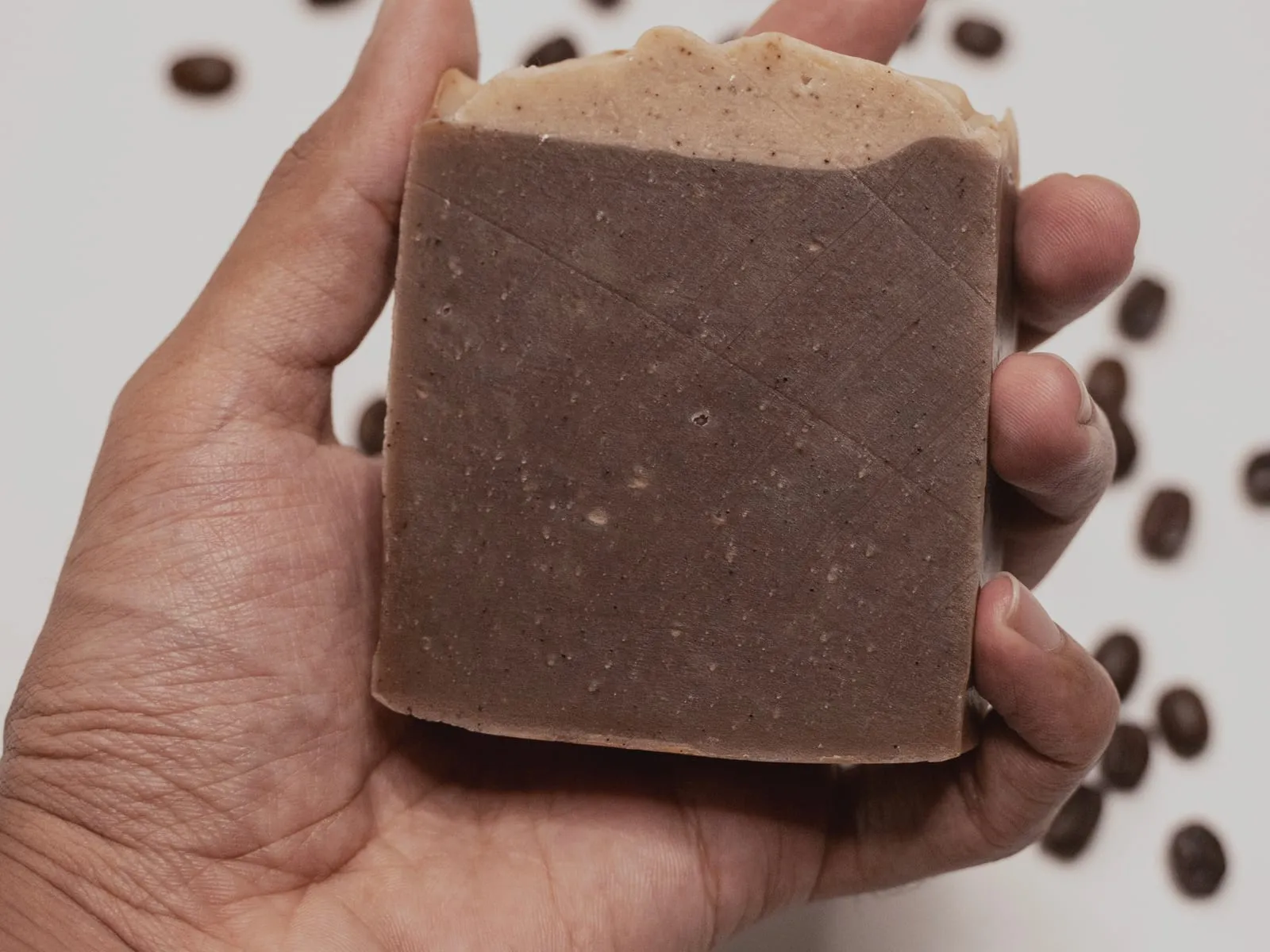 A hand holding a brown coffee soap bar with a scored criss-cross face.